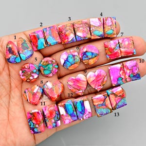 May include: A collection of colorful gemstone cabochons in various shapes, including teardrops, rectangles, squares, circles, and hearts. The stones feature a mix of pink, red, blue, turquoise, and gold colors, with a polished, glossy finish. These gemstones are ideal for jewelry making.