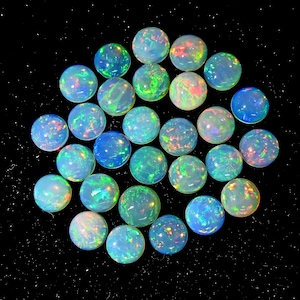 May include: A collection of round opals, each displaying a play of color with iridescent flashes of blue, green, and red. The opals are set against a black background, highlighting their vibrant hues and spherical shape. These gemstones are ideal for jewelry making.