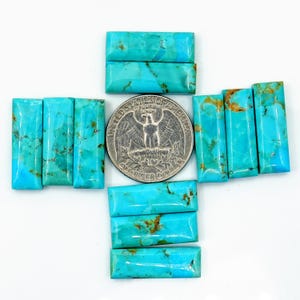 May include: A collection of rectangular turquoise gemstones with natural matrix patterns, arranged around a US quarter coin. The gemstones display shades of blue and green, with brown veining. The quarter coin features an eagle design.