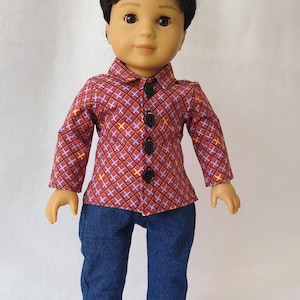 May include: A doll wearing a red and blue checked shirt with black buttons, blue jeans, and teal blue trainers.