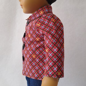 May include: A doll wearing a red, blue and yellow patterned shirt with a button-up closure and blue jeans.
