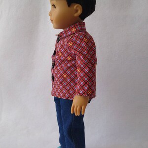 May include: A doll wearing a red and blue checked shirt with yellow accents, blue jeans, and teal shoes.