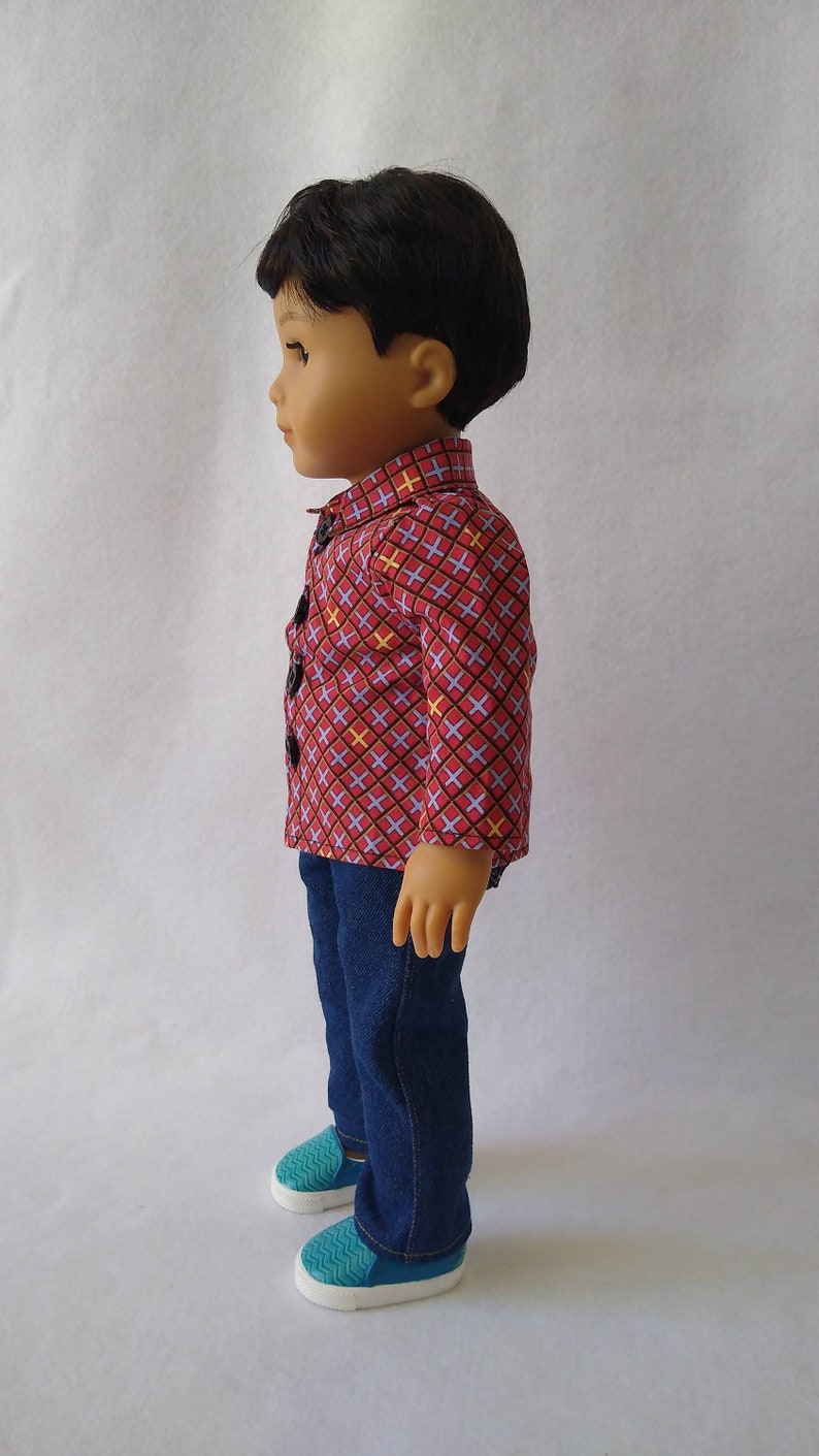 May include: A doll wearing a red and blue checked shirt with yellow accents, blue jeans, and teal shoes.