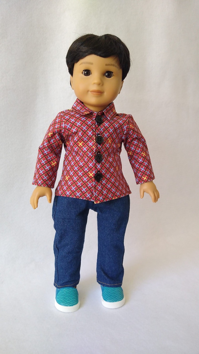 May include: A doll wearing a red and blue checked shirt with black buttons, blue jeans, and teal blue trainers.