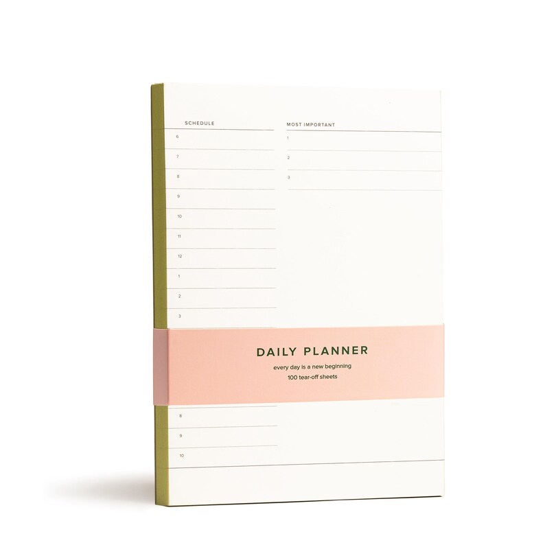 Puede incluir: Un bloc de notas de planificaci&oacute;n diaria con una cubierta rosa y verde. El bloc de notas tiene 100 hojas de papel que se pueden arrancar y dice "DAILY PLANNER" y "every day is a new beginning" en la cubierta.