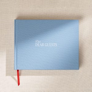May include: A light blue guest book with the words "Our Dear Guests" in white script. The book has a red ribbon bookmark. The cover has a textured appearance.