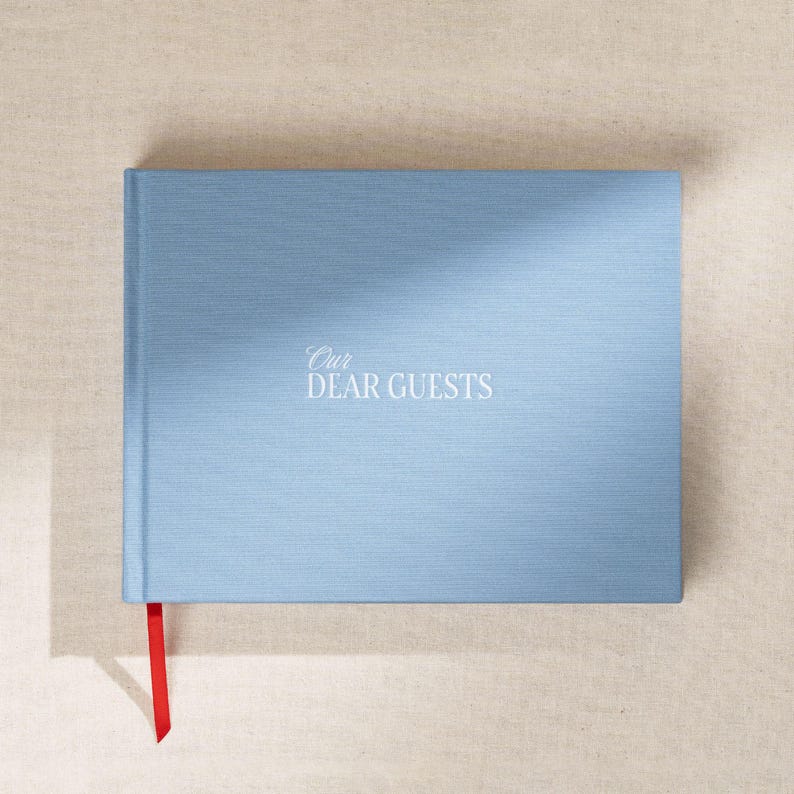 May include: A light blue guest book with the words "Our Dear Guests" in white script. The book has a red ribbon bookmark. The cover has a textured appearance.