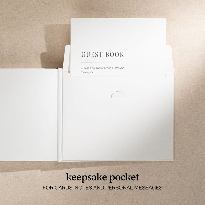 May include: A white guest book with a pocket for cards and notes. The book is open, revealing a card that reads "GUEST BOOK" and "PLEASE SIGN AND LEAVE US A MESSAGE THANK YOU." The bottom of the book reads "keepsake pocket FOR CARDS, NOTES AND PERSONAL MESSAGES."