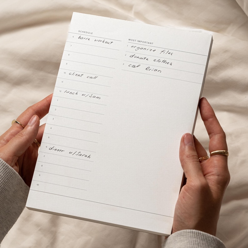 Puede incluir: Un bloc de notas blanco con una lista de tareas pendientes en negro. La lista incluye "barre workout", "client call", "lunch w/Sam" y "dinner w/Sarah". La secci&oacute;n m&aacute;s importante incluye "organize files", "donate clothes" y "call Brian".