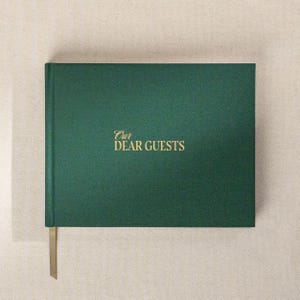 May include: A dark green guest book with the gold text "Our Dear Guests" on the cover. The book has a matching green ribbon bookmark. The book is rectangular and has a textured cover.