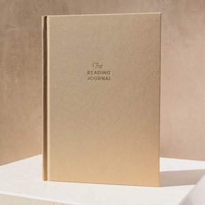 May include: A gold-coloured journal with the text "The Reading Journal" embossed on the front cover.