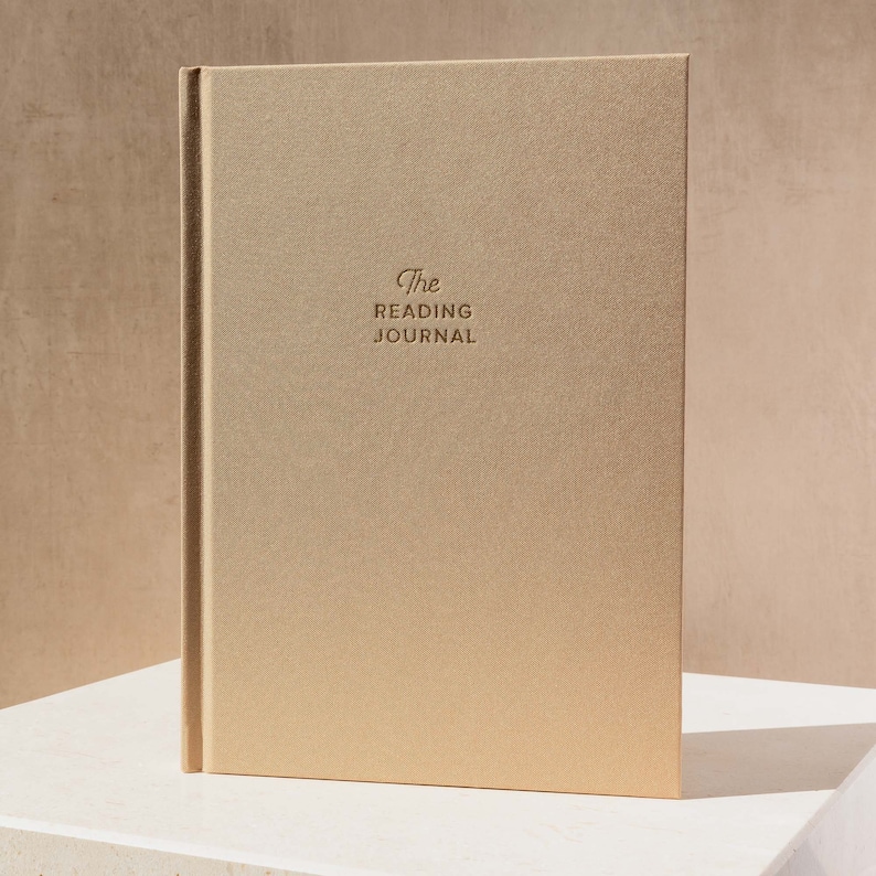 May include: A gold-coloured journal with the text "The Reading Journal" embossed on the front cover.