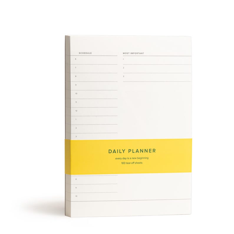Puede incluir: Un bloc de notas blanco con una franja amarilla en la parte inferior. El bloc de notas tiene un dise&ntilde;o de planificador diario con el texto "DAILY PLANNER" y "every day is a new beginning". El bloc de notas tambi&eacute;n tiene el texto "100 tear-off sheets".