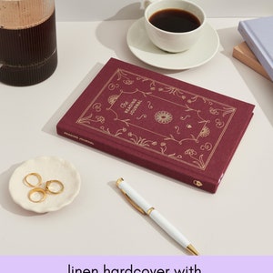 May include: A burgundy linen hardcover journal with gold foil accents and the text "The Reading Journal" on the front cover.