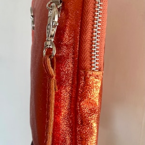 May include: A metallic orange clutch with a silver zipper and hardware. The clutch has a wrist strap and a textured surface. The zipper is a light orange color.