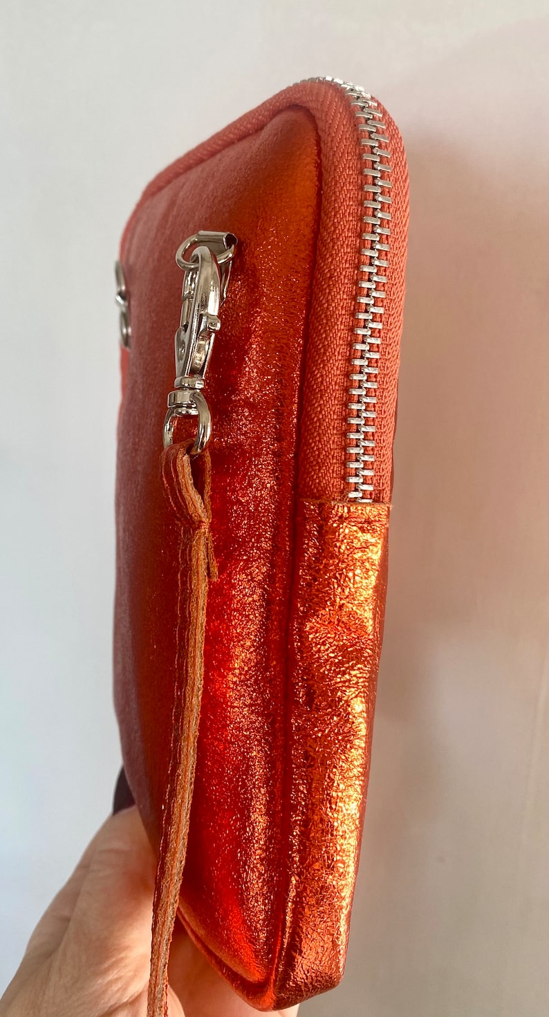 May include: A metallic orange clutch with a silver zipper and hardware. The clutch has a wrist strap and a textured surface. The zipper is a light orange color.