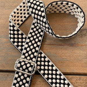 May include: Black and white patterned strap with a silver-colored metal buckle. The strap features a repeating dot pattern in black against a white background. The strap is made of a woven material.