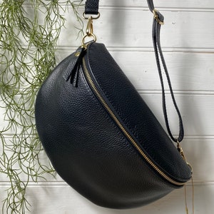 May include: Black leather crossbody bag with a gold zipper and hardware. The bag has a curved shape and an adjustable strap. A small tag with the letters "RR" hangs from the bag.