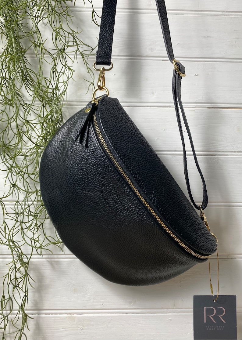 May include: Black leather crossbody bag with a gold zipper and hardware. The bag has a curved shape and an adjustable strap. A small tag with the letters "RR" hangs from the bag.