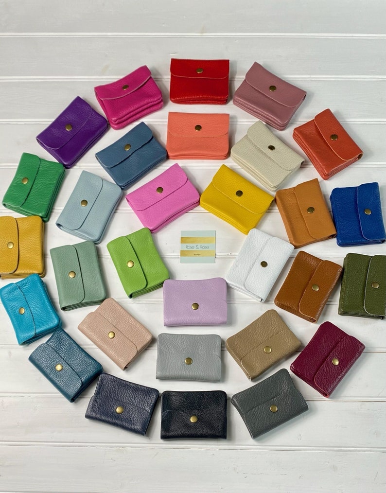 May include: A collection of small, colorful leather wallets arranged in a circular pattern. The wallets come in various colors, including red, pink, blue, green, and yellow. Each wallet has a flap closure with a gold-colored snap.