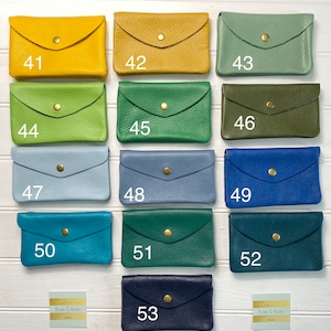 May include: A collection of small, leather wallets in various colors, including yellow, green, blue, and navy. Each wallet has a flap closure with a gold-colored snap. The wallets are numbered from 41 to 53.