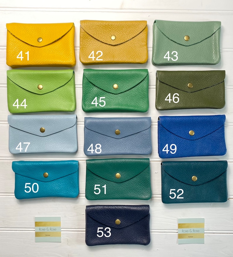 May include: A collection of small, leather wallets in various colors, including yellow, green, blue, and navy. Each wallet has a flap closure with a gold-colored snap. The wallets are numbered from 41 to 53.