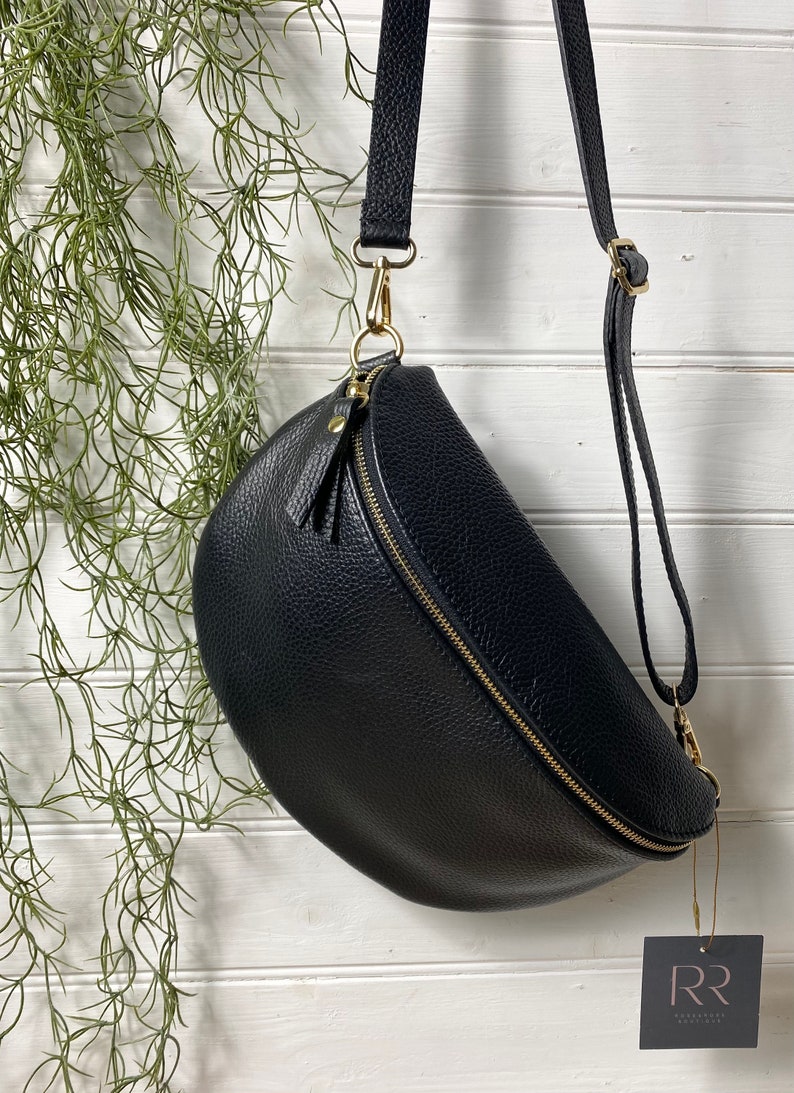 May include: Black leather crossbody bag with a gold zipper and hardware. The bag has a curved shape and a long adjustable strap. A small tag with the letters "RR" hangs from the bag.