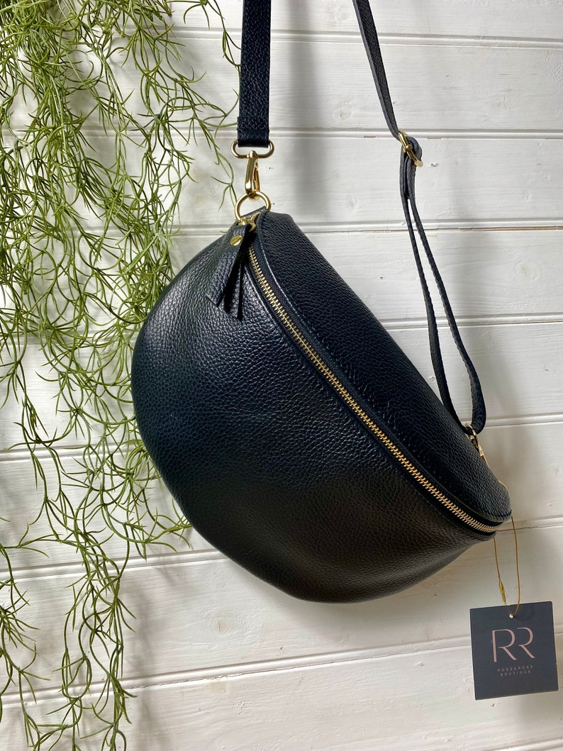 May include: A navy blue, crescent-shaped crossbody bag with a gold zipper and hardware. The bag has a textured leather appearance and a long, adjustable strap. A small tag with the letters "RR" hangs from the bag.