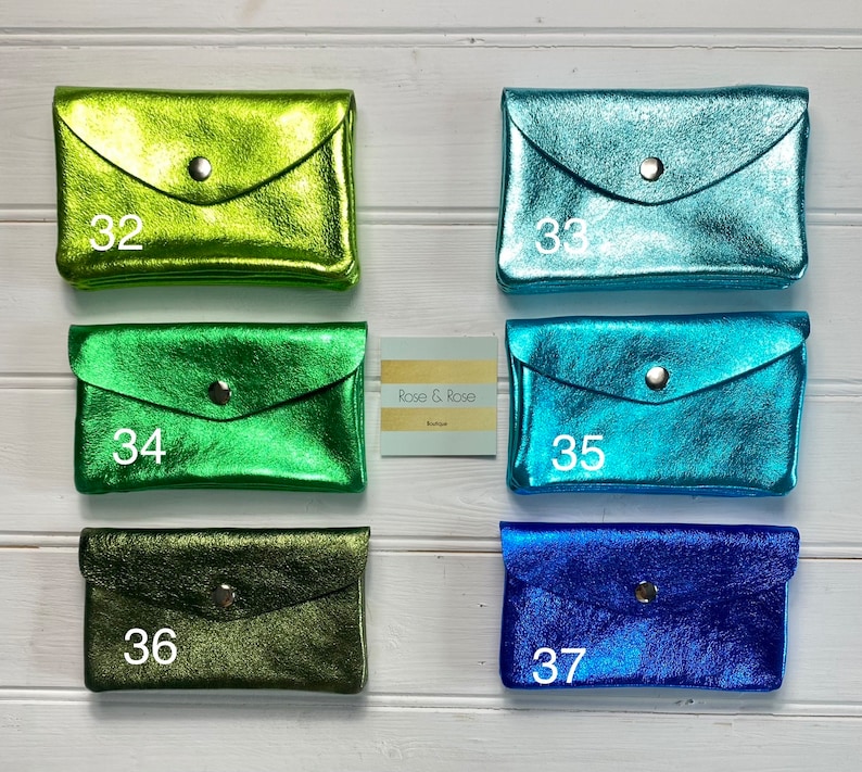 May include: Six metallic leather wallets in shades of green, teal, and blue are displayed. Each wallet features a flap closure with a silver popper. The wallets are numbered 32 to 37. The brand name "Rose & Rose" is also visible.