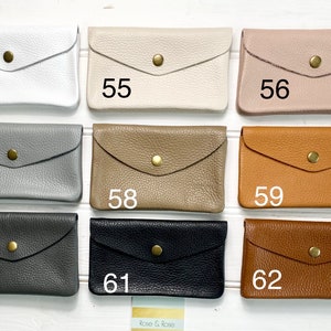 May include: A collection of leather wallets in various colors, including white, beige, pink, gray, tan, brown, black, and dark brown. Each wallet has a flap closure secured by a gold-colored snap. Numbers 54 through 62 are printed on the wallets.