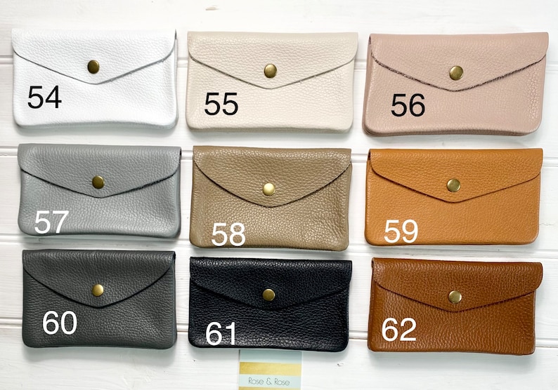 May include: A collection of leather wallets in various colors, including white, beige, pink, gray, tan, brown, black, and dark brown. Each wallet has a flap closure secured by a gold-colored snap. Numbers 54 through 62 are printed on the wallets.