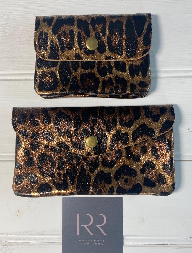 May include: Two leopard print clutch purses with gold-coloured hardware. The purses are in different sizes, with a small square purse on top and a larger rectangular purse below. The purses have a gold-coloured button closure.