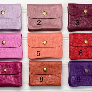 May include: Nine small, leather coin purses in various colors: lavender, mauve, burgundy, hot pink, coral, red, fuchsia, burnt orange, and purple. Each purse has a flap closure with a gold-colored snap.
