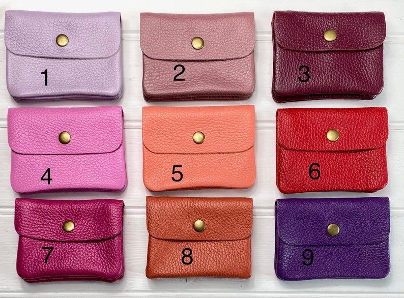 May include: Nine small, leather coin purses in various colors: lavender, mauve, burgundy, hot pink, coral, red, fuchsia, burnt orange, and purple. Each purse has a flap closure with a gold-colored snap.