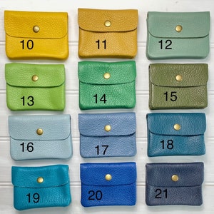 May include: A collection of small, leather coin purses in various colors, including yellow, green, blue, and teal. Each purse has a flap closure with a gold-colored snap. Numbers 10 through 21 are printed on the purses.