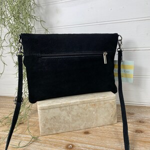 May include: A black suede crossbody bag with a silver chain strap. The bag has a zipper closure and a small tag that says "Rose & Rose". The bag is sitting on a marble-like box.
