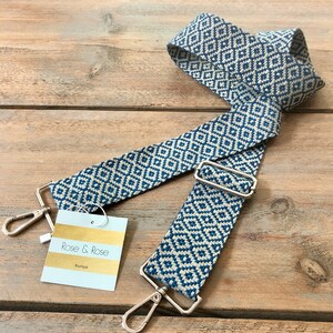 May include: A blue and cream patterned bag strap with silver-tone metal fixings. The strap has a geometric diamond design and includes a tag that reads "Rose & Rose Boutique".