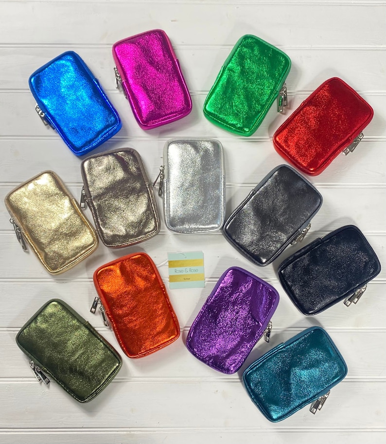 May include: A collection of metallic-finish phone cases in various colors, including blue, pink, green, red, gold, silver, black, olive, orange, purple, and teal. Each case has a rectangular shape with a zipper closure. A small tag with the text "Rose & Rose" is also visible.