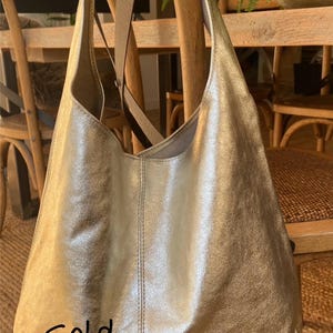 May include: A gold-colored leather tote bag with a shoulder strap. The bag is hanging on a wooden chair. The word "Gold" is written on the bag.