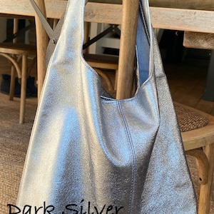 May include: A dark silver tote bag with a shoulder strap, hanging on a wooden chair. The bag has a textured metallic finish and a stitched seam down the center. The text "Dark Silver" is visible on the bag.