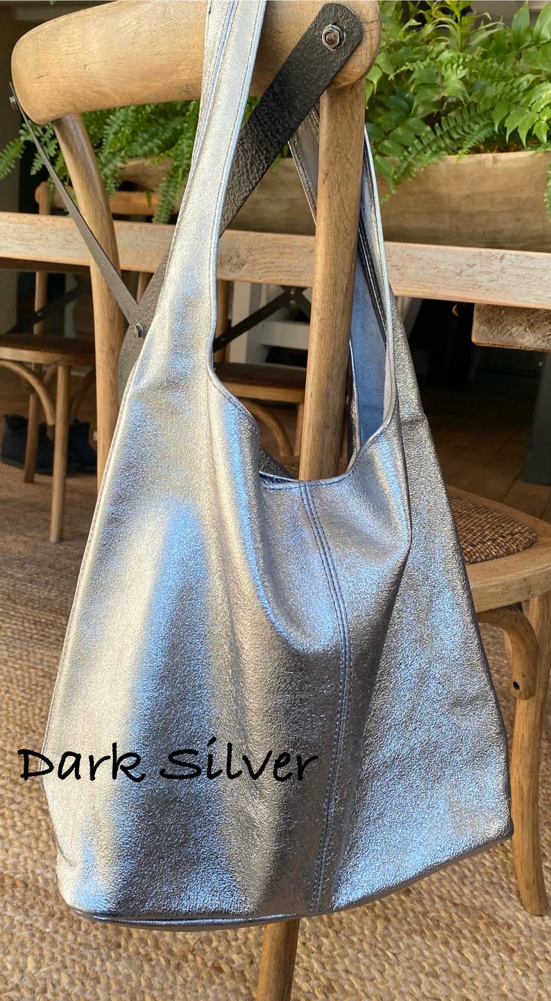 May include: A dark silver tote bag with a shoulder strap, hanging on a wooden chair. The bag has a textured metallic finish and a stitched seam down the center. The text "Dark Silver" is visible on the bag.