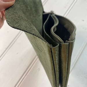 May include: An olive green leather wallet with multiple compartments and a zip closure. The wallet has a textured surface and a flap closure. The interior is visible, showing the different sections for organisation.
