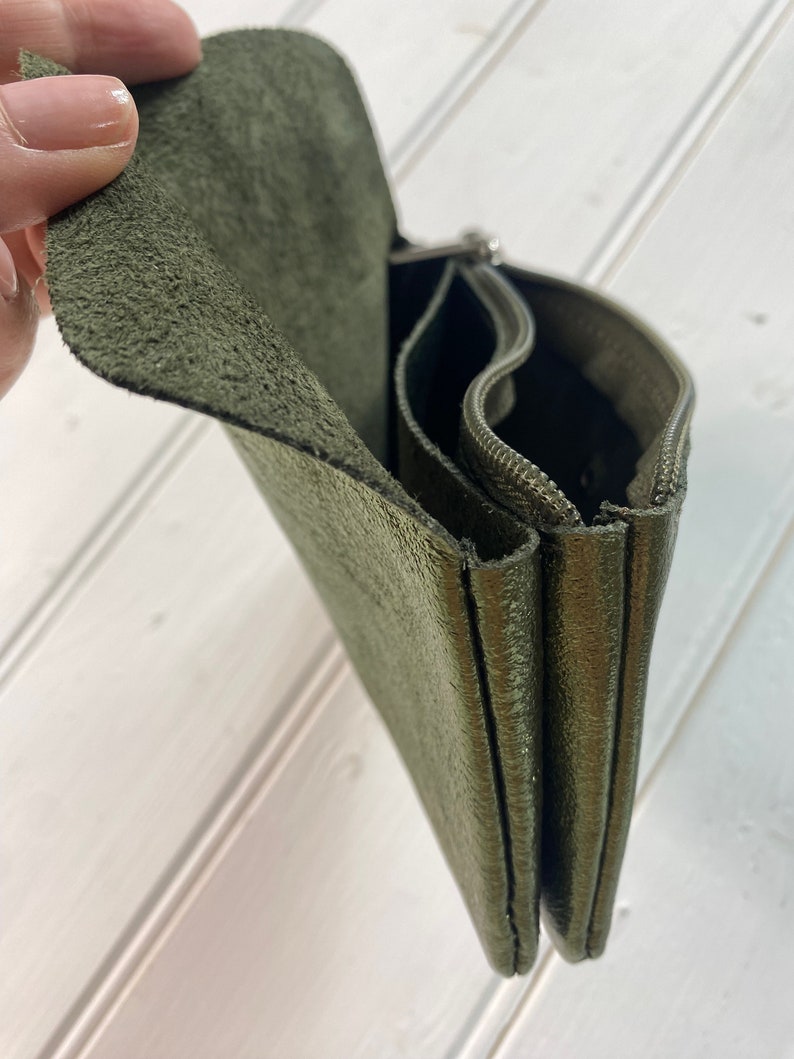 May include: An olive green leather wallet with multiple compartments and a zip closure. The wallet has a textured surface and a flap closure. The interior is visible, showing the different sections for organisation.