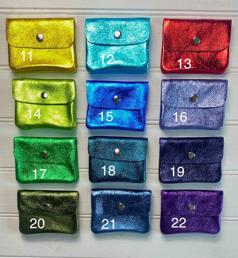 May include: A selection of small, metallic coin purses in various colours, including gold, teal, red, blue, and purple. Each purse has a flap closure with a silver snap. Numbers 11 to 22 are printed on the purses.
