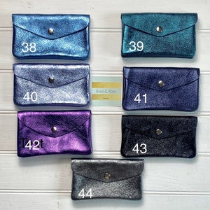 May include: A selection of small, metallic wallets in shades of blue, teal, purple, and black. Each wallet features a flap closure with a silver press stud. The wallets are displayed on a white wooden surface. Numbers 38, 39, 40, 41, 42, 43, and 44 are printed on the wallets.