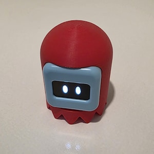 May include: A red, 3D-printed robot toy with a light blue faceplate. The robot has two glowing white dots for eyes and a jagged, pointed base. The toy is designed to resemble a popular video game character.