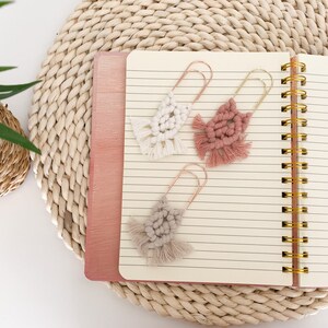 May include: Three handmade macrame bookmarks with gold metal clips. The bookmarks are in shades of pink and cream.