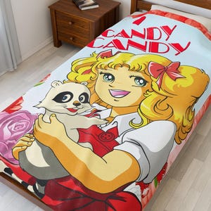 May include: A light blue and red Candy Candy blanket featuring a cartoon illustration of a blonde girl holding a raccoon. The blanket has the words "Candy Candy" in red. Floral and rose accents are visible.