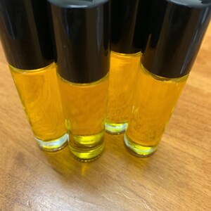 May include: Several roll-on bottles filled with a golden-yellow liquid. Each clear glass bottle has a black cap. The bottles are arranged on a wooden surface, with the light reflecting off the glass and liquid.