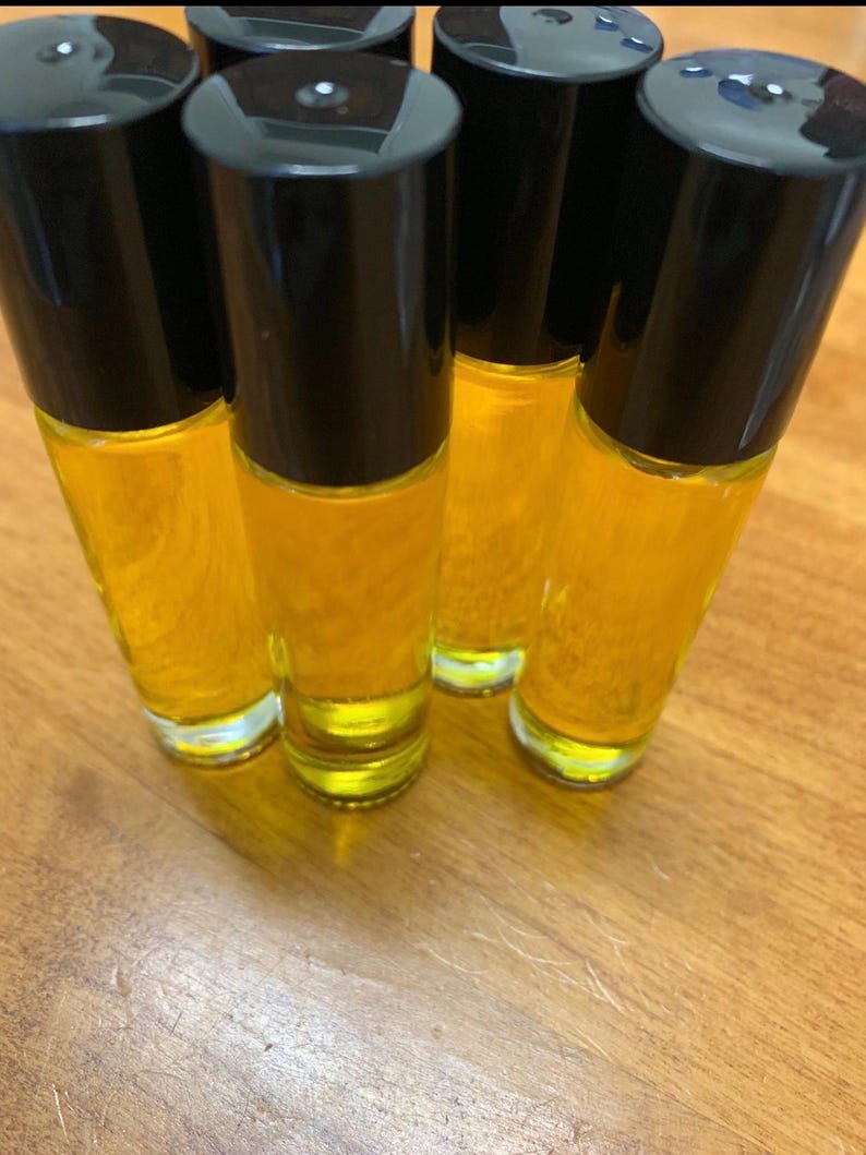 May include: Several roll-on bottles filled with a golden-yellow liquid. Each clear glass bottle has a black cap. The bottles are arranged on a wooden surface, with the light reflecting off the glass and liquid.